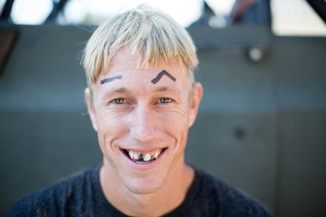 Portrait of young man with badly cut hair, drawn on eyebrows and blacked out teeth