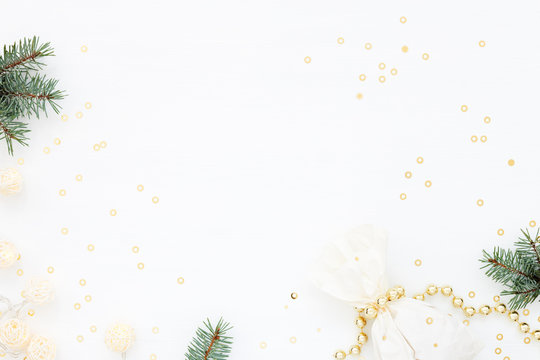 Bright Christmas composition with a gift & New Year decoration. Gold pearl beads, fir,  paper bag, garland and confetti on white. Flat lay. Winter holiday card