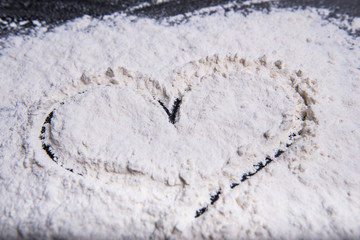Heart painted with finger in wheat meal on a grey working surface