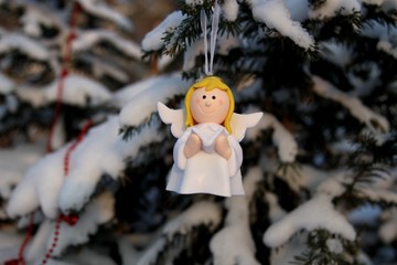 Angel with a book in his hands on a snow-covered branch in the park