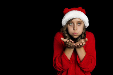 A young girl in a red sweater and a Santa Claus hat blows on her hands and looks at the viewer