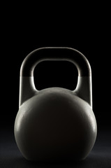 Naklejka na ściany i meble Backlit competition kettlebell silhouette on a black background with text / writing / copy space on and above kettlebell