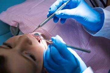 Dentist holding medical equipment while examining cute boy