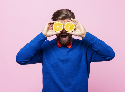 Man holding two half of orange in front of eyes .