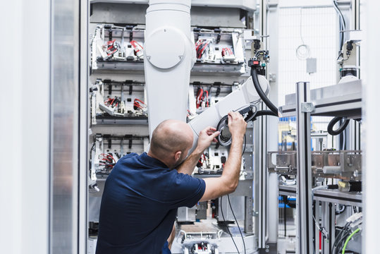Man working at industrial robot in modern factory - Powered by Adobe