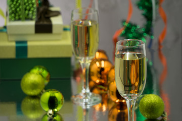 Two champagne glasses and christmas basket bottle, gifts with red satin ribbon, apples candy canes, pine cones branches, golden ornaments garlands on black wall background new year celebration concept