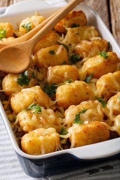 Delicious Baked Tater Tots with cheese, meat and greens close up in a dish baking dish. vertical
