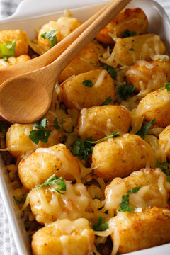 Casserole of Tater Tots with cheese and herbs close up in a dish baking dish. vertical