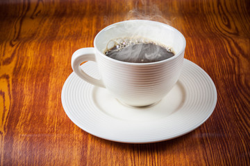 Hot coffee in white cup on wooden floor.