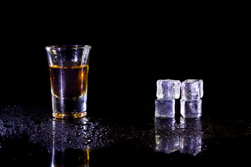 Whiskey in glass shots  with ice cubes on black background.