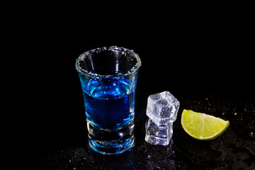 Cocktail blue shots with salt and lime, ice cubes on black background.