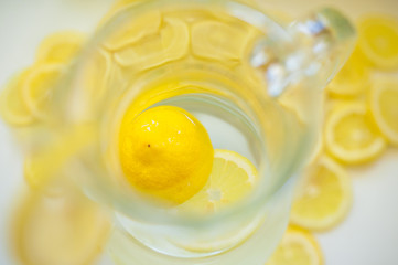 Pitcher with water and lemon next to slices of yellow lemon