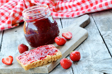 Jar of strawberry jam and fresh strawberries on wooden table
