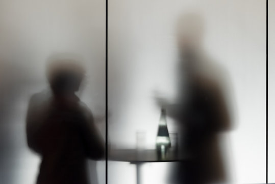 Konferenzteilnehmer machen eine Pause an einem Stehtisch hinter mattiertem Glas