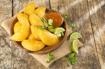 Colombian empanada with spicy sauce on wooden background