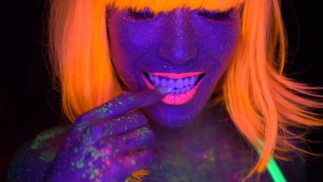 Closeup woman face and torso with fluorescent make up in orange, wig, creative makeup look great for nightclubs. Halloween party, shows and music concept