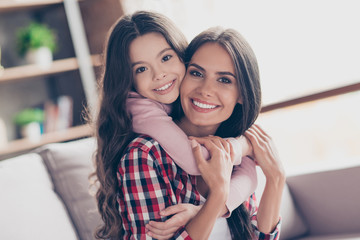 Time of tenderness. Beautiful young smiling mum and her little preteen daughter are spending time together. They are hugging and playing games at home