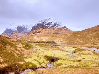 Stream and stony bridge  in spring Hiigland mountains in Scotland. Snowy mountains in heavy clouds.