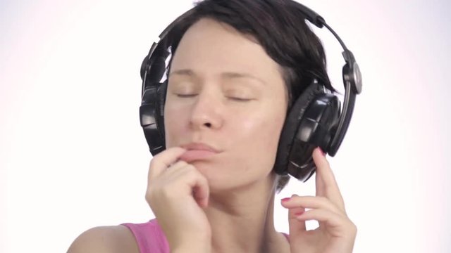 Beautiful woman dancing in headphones while listening to a music on a light background