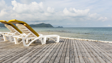 Fototapeta na wymiar Beach bed on natural wooden floor platform which located beside the clean and clear water in ocean, with white cloud and blue sky as background at skyline.