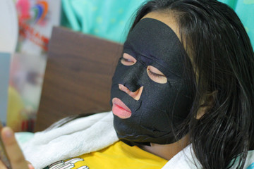 young beautiful woman is having a black mask on her skin.Skin health. Black Mask on Woman Face.