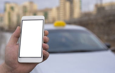 Close-up of a hand of a man holding a mobile phone in the background of a car and a city, booking a taxi. Mock up a clean smartphone screen for the design of your advertisement.