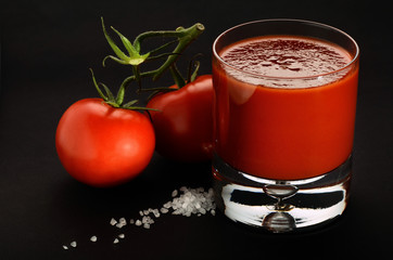Tomato juice decorated with tomatoes and salt on black background