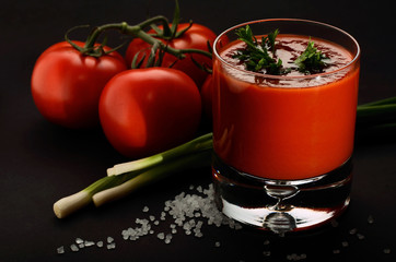 Tomato juice decorated with parsley, onions and tomatoes on black background