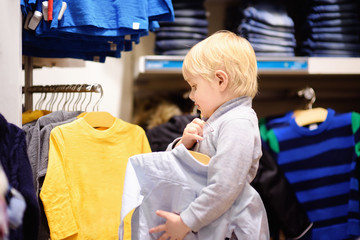 Cute little boy choosing new clothes during shopping