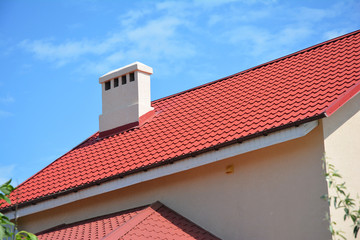 Beautiful red metal roof with roof gutter, fascia, ventilation and chimney. House roofing construction.