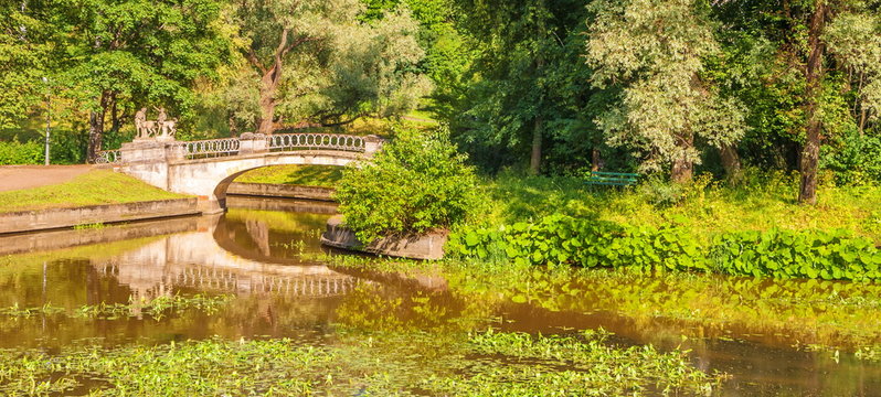 Ancient bridge with centaur sculptures over lake in summer park