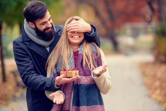 Young Hipster Man Wants To Surprise Girlfriend  With A Gift For Valentines Day Covering Her Eyes