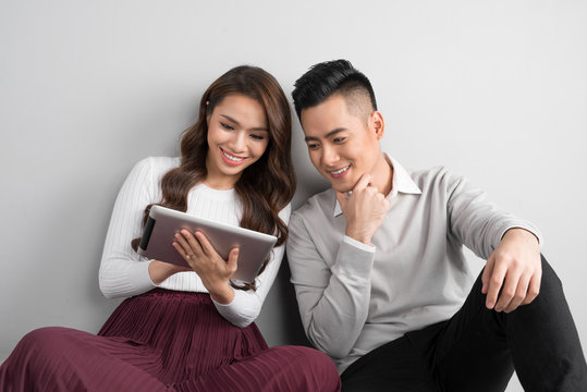 Pretty Smiling Asian Couple In Love Together Sitting On Floor Enjoying Using Digital Tablet