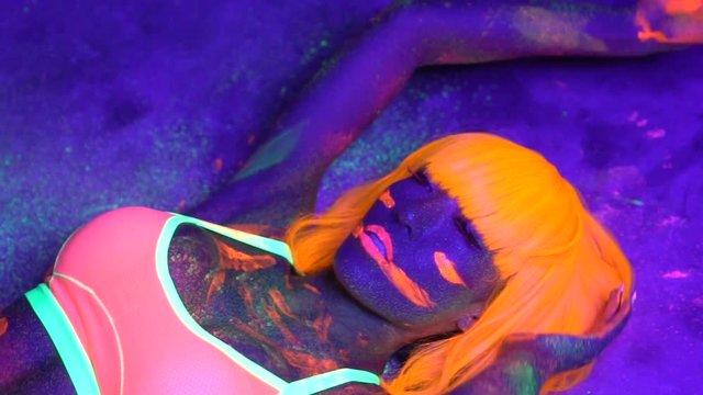 Sexy woman with fluorescent make up face and body in orange wig, creative makeup look great for nightclubs. Halloween party, shows and music concept - slow motion video