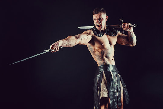 Furious muscular man posing shirtless with dangerous weapon and screaming in dark.