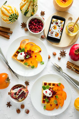 Plates of Belfian waffles with persimmon, pomegranate seeds and sour cream on white table cloth