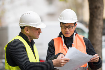 Young Asian apprentice at work on construction site with senior engineer. Outdoors