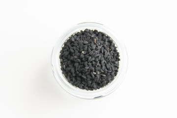 Kalonji (Black cumin) seeds called black nigella sativa or black cumin seeds in glass jar scattered on white background. Healthy vegan and vegetarian diet; super seeds. 