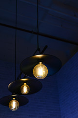 Tungsten black lamp glowing electric light bulbs on the ceiling with dark blue wall