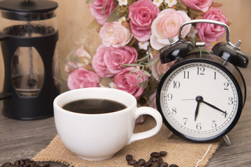 Fototapeta na wymiar Hot cup of coffee and alarm clock on wood table with rose flower.