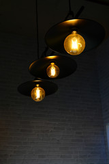 Tungsten black lamp glowing electric light bulbs on the ceiling with dark wall. Copy space