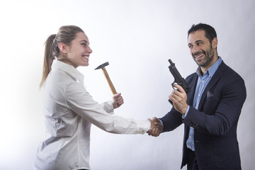 Una donna manager con un martello stringe la mano a un altro manager con una pistola  in giacca - sfondo chiaro - obrazy, fototapety, plakaty