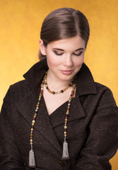 Portrait of beautiful young woman in a brown cloak with beads on the neck. The gaze is directed to the bottom, with a slight smile