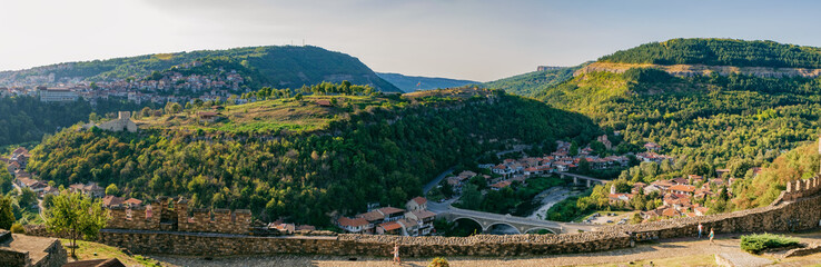 Fototapeta na wymiar Panoramic view of Veliko Tarnovo from Tsarevets hill. Medieval ruins of Tsarevets fortress and typical terrace architecture in Veliko Tarnovo, Bulgaria