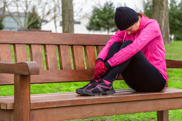 Female athlete tired or depressed resting on a bench on a cold winter day on the training track of...