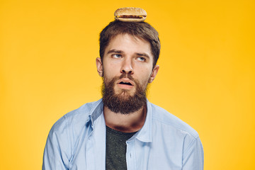 Young guy with a beard on a yellow background holds a hamburger