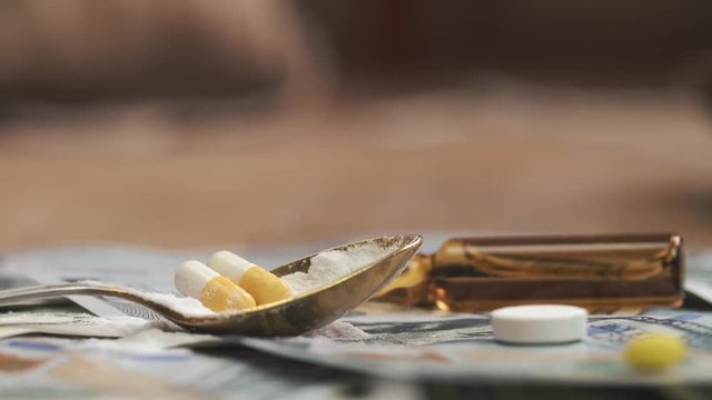 Spoon with cocaine, medicine pills on dollar bank notes 