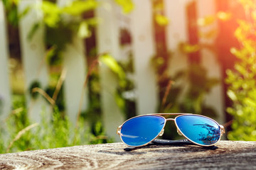 Fototapeta na wymiar Beautiful sunglasses in gold frame close-up. Lie on a wooden table in the background of a blurred greens. The concept of vacation, vacation, summer, vacation, travel. Copy space.