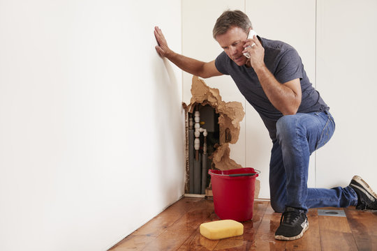 Middle aged man with a burst water pipe phoning for help