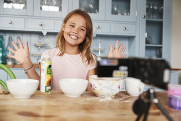 Girl video blogging in the kitchen smiling and showing hands